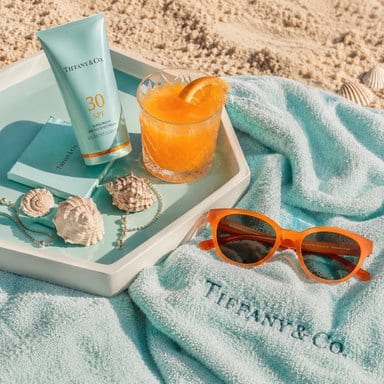 Flat-lay of sunscreen, sunglasses and a drink on a beach towel